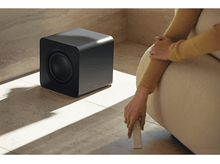Charger l&#39;image dans la galerie, Caisson de basses noir à côté d&#39;une personne avec une télécommande.
