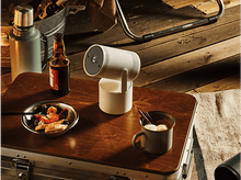 Charger l&#39;image dans la galerie, Un projecteur blanc sur une table en bois avec de la nourriture, de la bière et un thermos, en extérieur.
