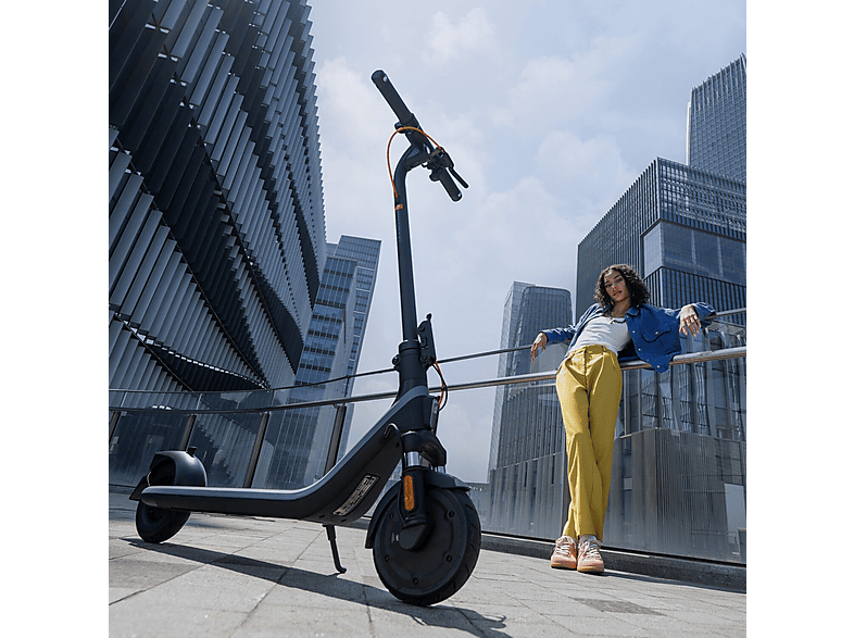 Une femme en pantalon jaune s'appuie sur une rampe à côté d'une trottinette électrique noire.
