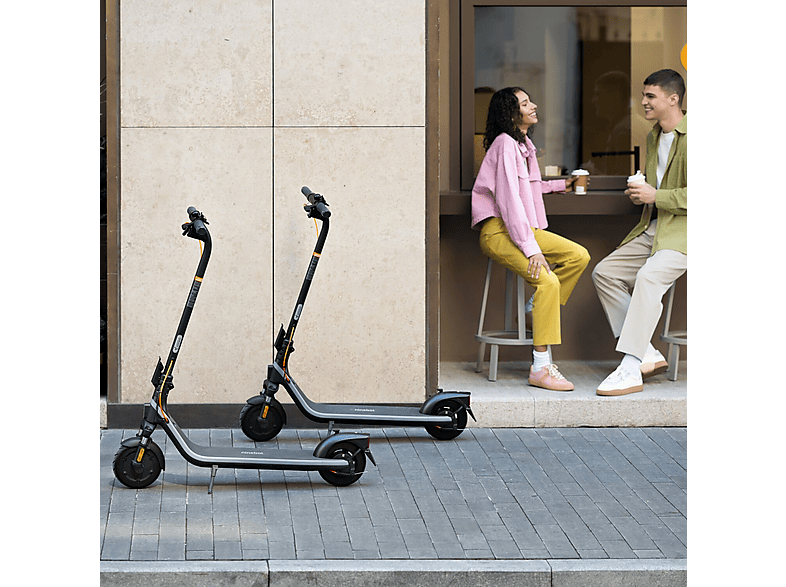 Deux scooters garés sur un trottoir. Un couple est assis à une table en arrière-plan.