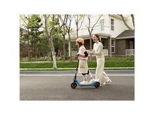 Charger l&#39;image dans la galerie, Une fille fait du scooter avec un adulte à côté, tous deux sur la route.
