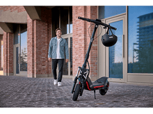 Charger l&#39;image dans la galerie, Homme marchant vers une trottinette électrique garée près d&#39;un bâtiment.
