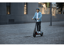 Charger l&#39;image dans la galerie, Un homme conduisant une trottinette électrique dans une rue.
