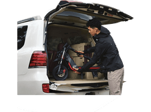 Charger l&#39;image dans la galerie, Homme chargeant une trottinette pliable dans un coffre de voiture dans un parc.
