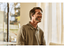 Charger l&#39;image dans la galerie, Homme avec écouteurs, souriant. Fond: fenêtre, feuillage vert.
