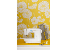 Charger l&#39;image dans la galerie, Une machine à coudre blanche sur une surface jaune avec du papier peint floral.
