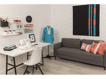 Charger l&#39;image dans la galerie, Une salle de couture avec une machine à coudre, des fournitures et un mannequin portant une tunique turquoise.
