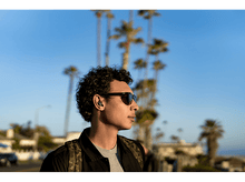 Charger l&#39;image dans la galerie, Un homme portant des lunettes de soleil et des écouteurs dans un environnement ensoleillé.
