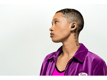 Charger l&#39;image dans la galerie, Une personne aux cheveux courts portant une veste violette avec des écouteurs dans l&#39;oreille, regardant à gauche.
