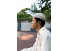 Charger l&#39;image dans la galerie, Homme avec écouteurs, portant un bonnet et une veste, dans un cadre ressemblant à un parc. Vue de profil.
