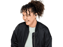 Charger l&#39;image dans la galerie, Une femme aux cheveux bouclés sourit tout en portant des écouteurs et une veste noire.
