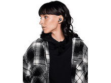 Charger l&#39;image dans la galerie, Une femme aux cheveux foncés portant des écouteurs, regardant vers la gauche, dans une chemise à carreaux.
