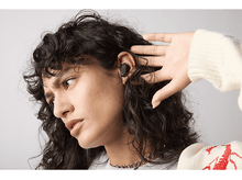 Charger l&#39;image dans la galerie, Femme portant un écouteur, ajustant l&#39;autre, regardant ailleurs.
