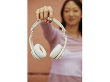 Charger l&#39;image dans la galerie, Femme tenant un casque blanc. Elle porte un haut rose. Arrière-plan flou avec un mur rose.
