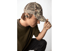 Charger l&#39;image dans la galerie, Un homme en casquette camouflage et chemise olive portant un écouteur noir, regardant vers le bas.
