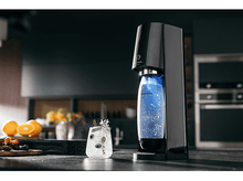 Charger l&#39;image dans la galerie, Une machine à soda avec une bouteille se remplissant de liquide bleu, un cocktail et des oranges sur un comptoir.
