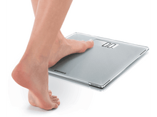 Charger l&#39;image dans la galerie, Une personne se tient sur une balance en verre. La balance affiche 0,0 kg. Fond blanc.
