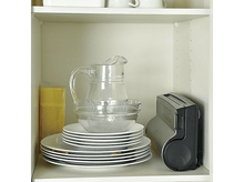 Charger l&#39;image dans la galerie, Étagère blanche avec verrerie, assiettes et une scelleuse alimentaire grise, éclairée d&#39;en haut.
