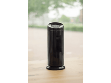 Charger l&#39;image dans la galerie, Un purificateur d&#39;air noir est posé sur une table en bois. L&#39;arrière-plan montre une fenêtre floue avec du feuillage vert et un bâtiment.
