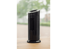 Charger l&#39;image dans la galerie, Un purificateur d&#39;air noir est posé sur une table en bois. Il a un design cylindrique avec des boutons de commande sur le dessus. Une fenêtre est en arrière-plan.
