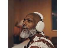Charger l&#39;image dans la galerie, Un homme avec une barbe grise portant un casque blanc regarde en l&#39;air, assis dans une pièce avec un mur marron.
