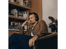 Charger l&#39;image dans la galerie, Un homme portant un casque est assis sur une chaise verte, l&#39;air pensif. Des bibliothèques sont en arrière-plan.
