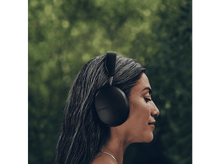 Charger l&#39;image dans la galerie, Une femme aux cheveux gris portant un casque SONOS noir sur un fond vert flou.
