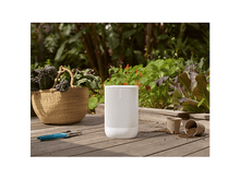 Charger l&#39;image dans la galerie, Un haut-parleur blanc est sur une terrasse en bois. Un panier de verdure, des cisailles et des pots sont également visibles.
