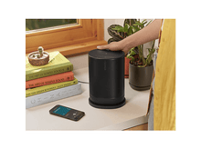 Charger l&#39;image dans la galerie, Haut-parleur noir, livres et téléphone sur une surface blanche. Une main touche le haut-parleur.
