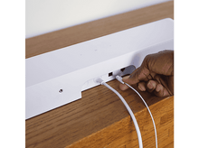 Charger l&#39;image dans la galerie, Une main branche un câble blanc dans une barre de son blanche. La barre de son est sur une surface en bois.
