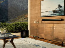 Charger l&#39;image dans la galerie, Un salon avec un meuble en bois, une télévision, une image de surf et une barre de son noire.
