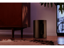 Charger l&#39;image dans la galerie, Caisson de basses noir à côté d&#39;une armoire en bois et d&#39;une plante.
