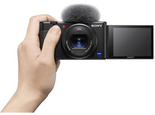 Charger l&#39;image dans la galerie, Une personne tenant un appareil photo noir avec un microphone sur le dessus et un écran ouvert.

