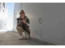 Charger l&#39;image dans la galerie, Une personne filmant avec une caméra dans un environnement urbain.
