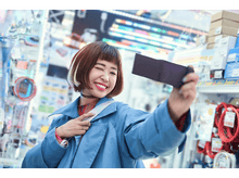 Charger l&#39;image dans la galerie, Une femme en manteau bleu prend un selfie dans une boutique, souriante.
