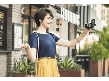 Charger l&#39;image dans la galerie, Femme prenant un selfie avec un appareil photo devant un bâtiment avec vue sur la rue.
