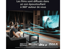 Charger l&#39;image dans la galerie, Des gens regardent une TV montrant un film de dinosaures. Les fonctionnalités sonores sont mentionnées.
