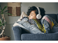 Charger l&#39;image dans la galerie, Femme sur un canapé avec un casque et une couverture, regardant pensivement vers la gauche.

