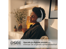 Charger l&#39;image dans la galerie, Une personne avec un casque, assise et souriante. Ils sont dans une pièce avec des plantes et du texte en dessous.
