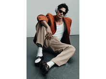 Charger l&#39;image dans la galerie, Homme en veste orange, lunettes de soleil et casque, assis par terre. Il porte un débardeur blanc, un pantalon beige et des mocassins.
