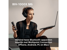 Charger l&#39;image dans la galerie, Une femme portant un casque, tenant un téléphone et un ordinateur portable. La scène est bien éclairée.
