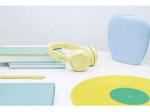 Charger l&#39;image dans la galerie, Une table avec un casque jaune, des livres, un stylo et un disque vinyle. Un vase bleu en arrière-plan.
