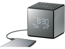 Charger l&#39;image dans la galerie, Réveil/radio numérique noir en forme de cube. Affiche l&#39;heure et le jour, et un téléphone en charge.
