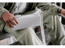 Charger l&#39;image dans la galerie, Une personne tenant un haut-parleur Sony gris clair, avec le nom de la marque dessus, assise sur des escaliers.
