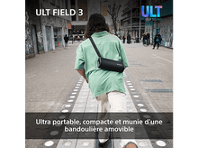Charger l&#39;image dans la galerie, Une personne marche dans la rue avec une enceinte Sony noire. Bâtiments et personnes en arrière-plan.
