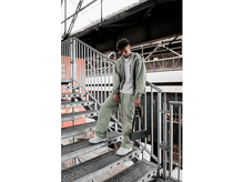 Charger l&#39;image dans la galerie, Un jeune homme descend un escalier en métal, tenant un haut-parleur noir.
