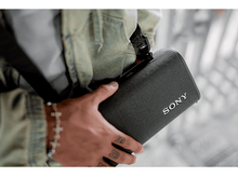 Charger l&#39;image dans la galerie, Une personne tenant une enceinte Sony grise avec le logo &#39;SONY&#39;, portant une veste en jean.
