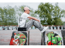 Charger l&#39;image dans la galerie, Un homme assis sur des blocs de béton avec un haut-parleur et un fond de graffiti.
