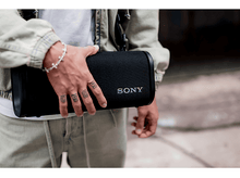 Charger l&#39;image dans la galerie, Une personne tenant une enceinte Sony noire avec le logo &#39;SONY&#39;, portant une veste en jean.
