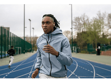 Charger l'image dans la galerie, Un homme courant sur une piste bleue, portant une veste bleu clair, un autre coureur derrière lui.
